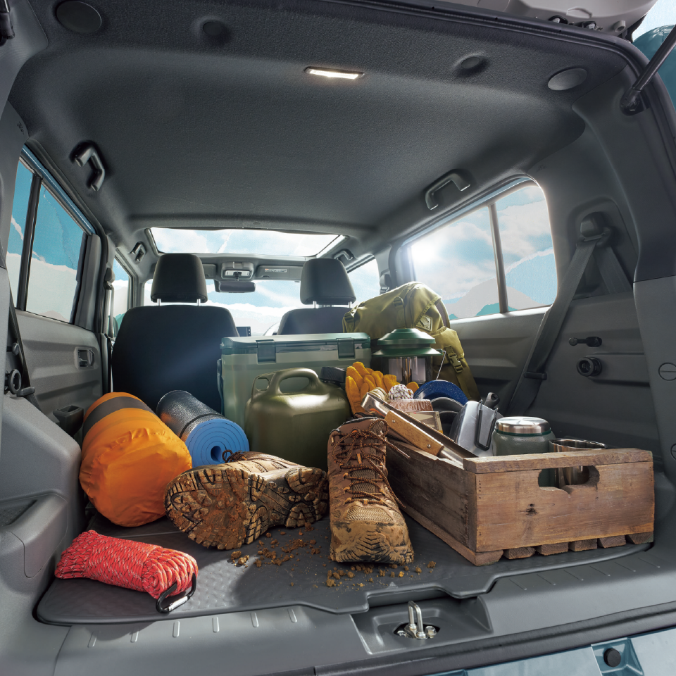 Hiking gear in a car trunk: boots, sleeping mat, backpack, crate with cookware, and water canister stored for a trip