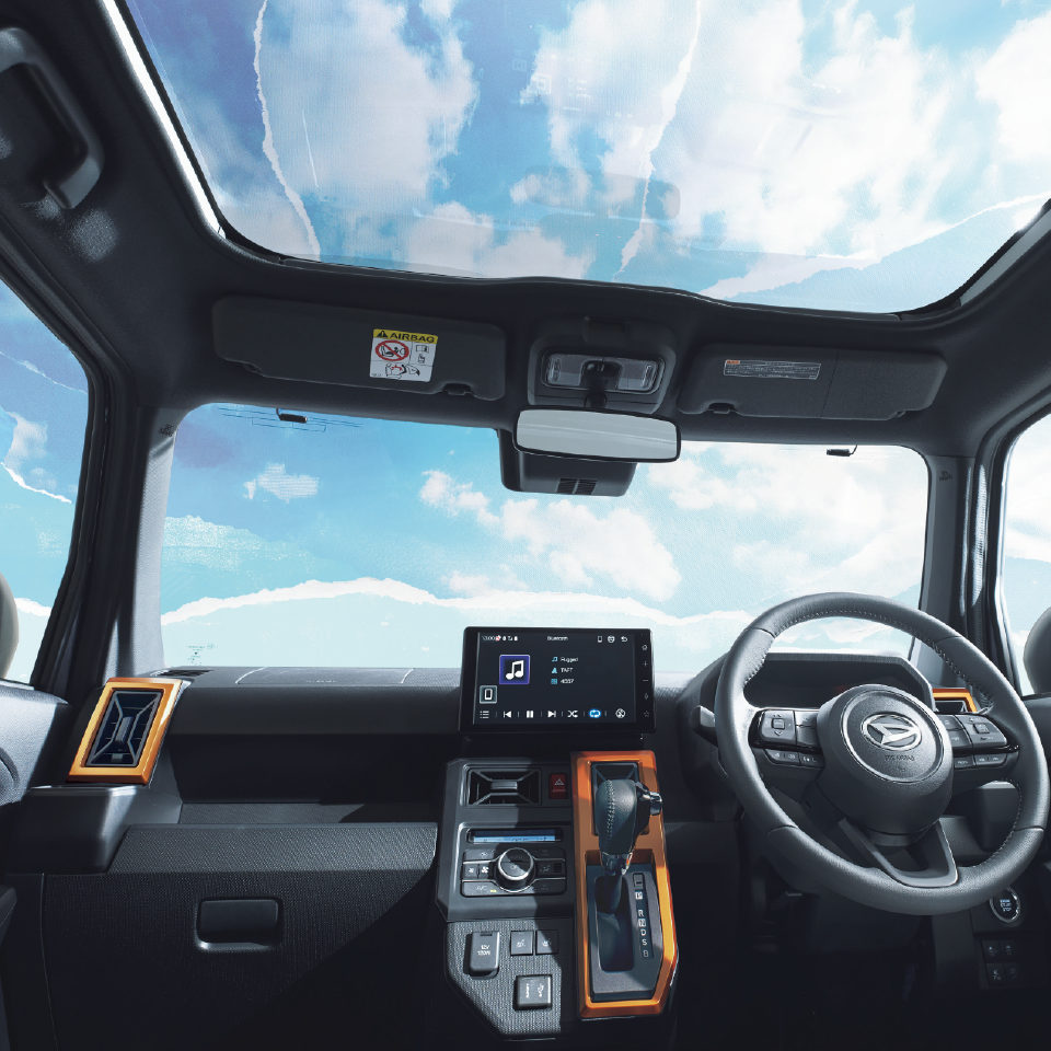 Interior of a modern car from the driver’s seat showing a steering wheel, center console, and large touchscreen display under a sunroof.