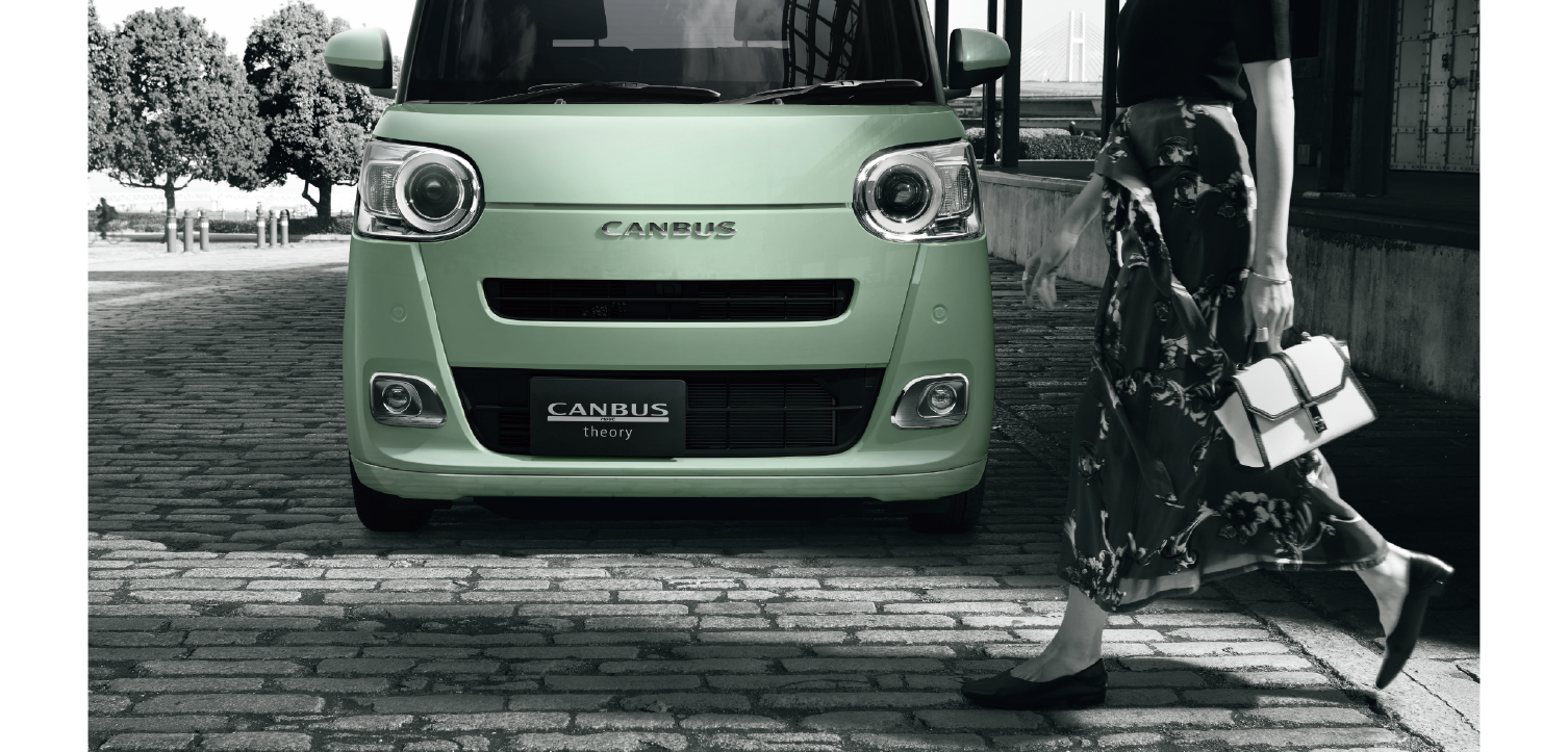 Front view of a mint-green Canbus van on a cobblestone street as a woman in a floral dress walks by with a white handbag.