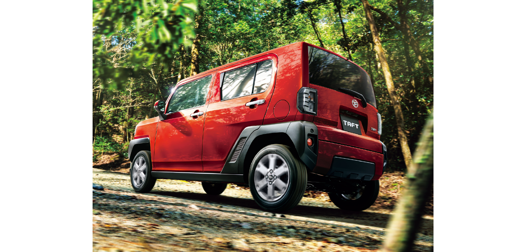 Red compact SUV driving on a dirt forest trail, trees and dappled sunlight in the background (Taft badge visible on rear).