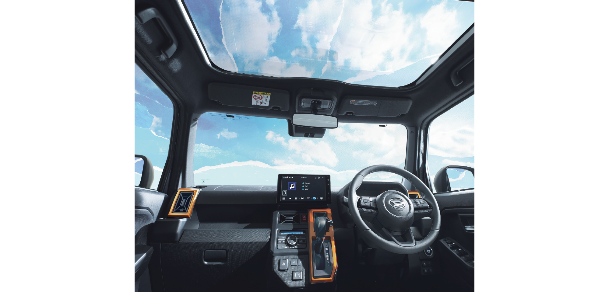 Car interior with a panoramic sunroof showing a blue sky and clouds; steering wheel and center console are in view.